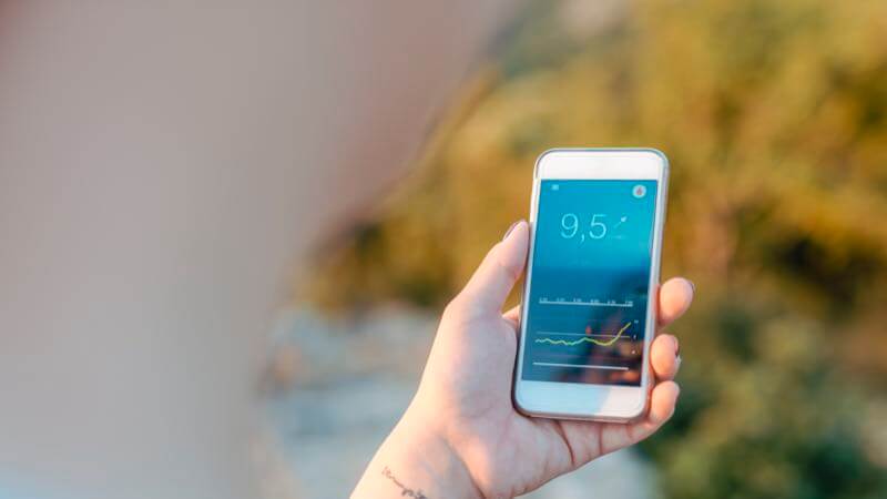Hand holding up a smartphone that shows a CGM reading