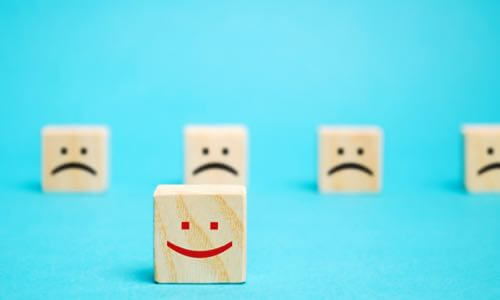 One wooden die with red smiley face in front & five wooden die with black frown faces in back