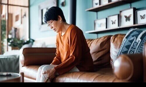 Diabetic Neuropathy Lower Extremities Woman sitting on a sofa looking down as she's massaging her leg